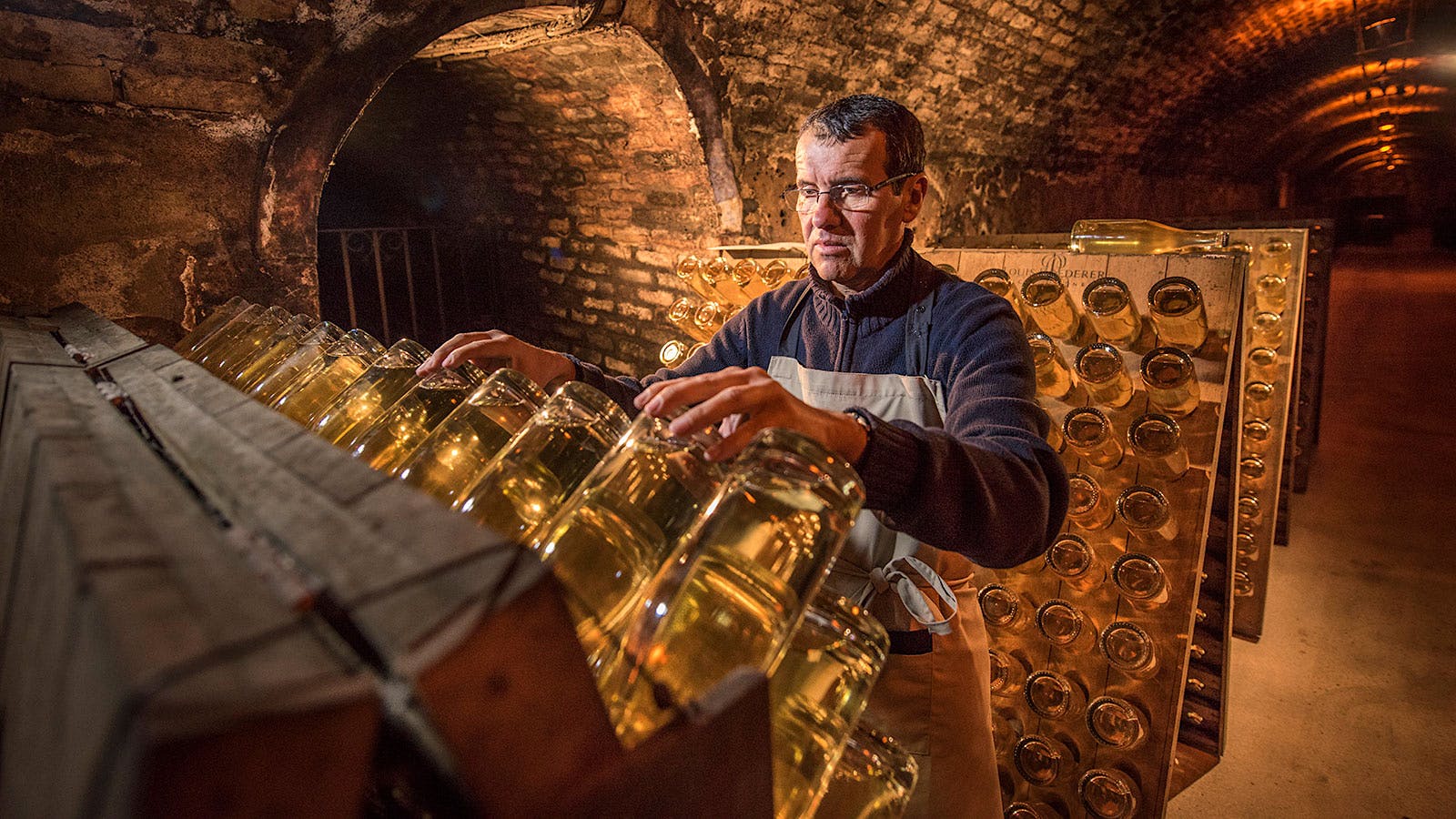 A man turning Champagne bottles in riddling racks in the caves of Champagne Louis Roederer