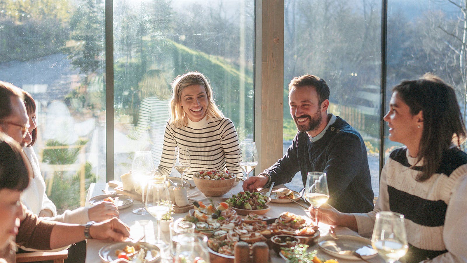 Group wearing sweaters at a dinner table, drinking white wine