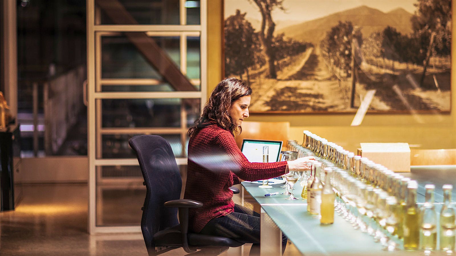 Quintessa’s Illumination winemaker Rebekah Wineburg sits at a desk with many unlabeled bottles of Sauvignon Blanc lined up in front of her as she catalogues and tastes each throughout the blending process.